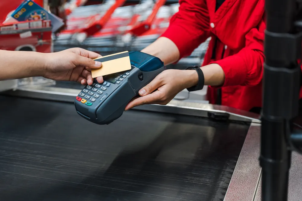 Credit card payment at retail checkout with POS terminal and cashier in red uniform