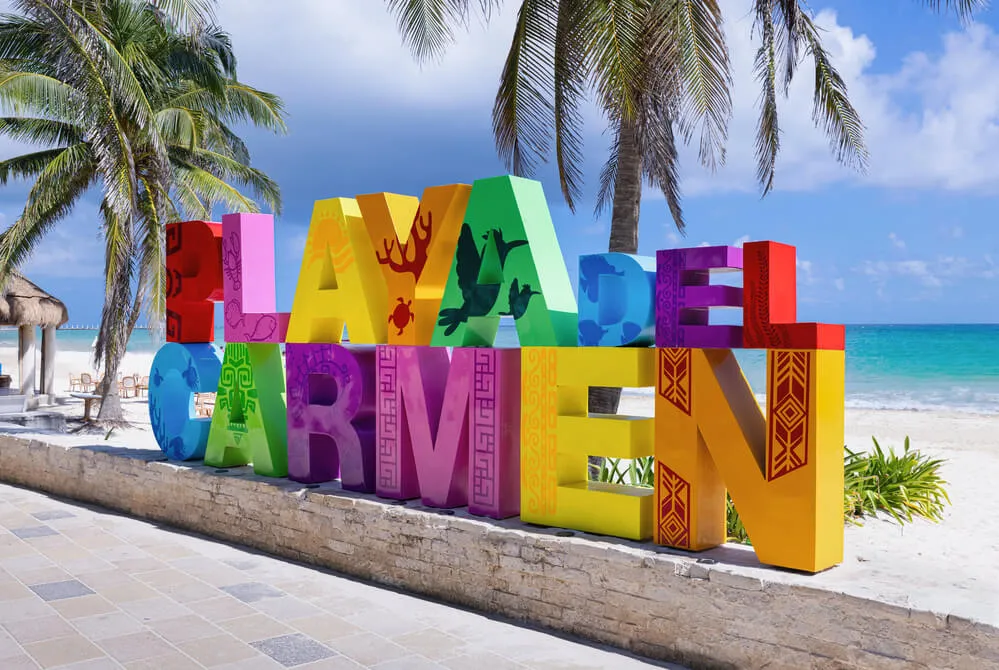 Colorful Playa del Carmen sign on beach promenade with turquoise sea and palm trees.