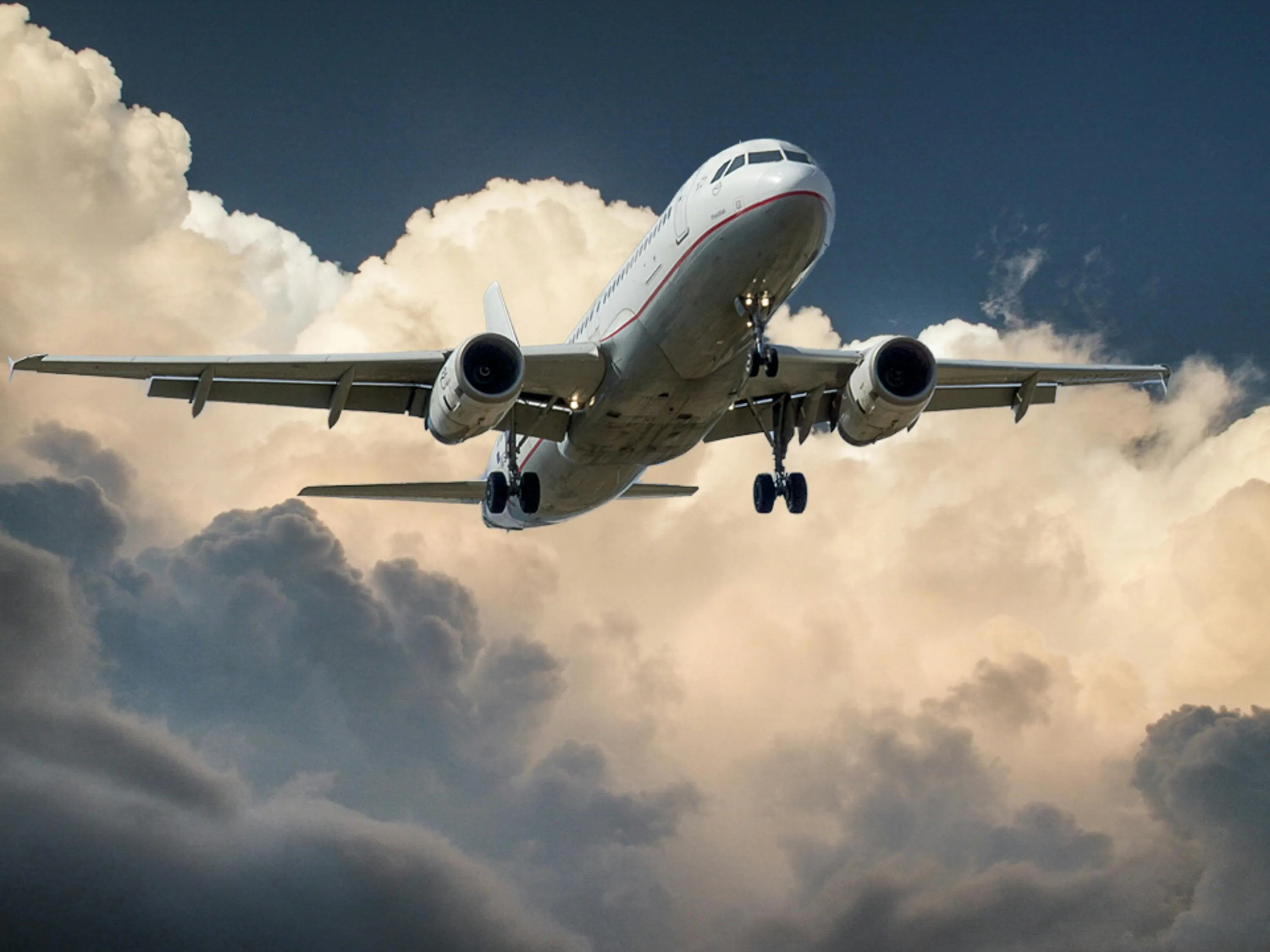 Wide-body commercial aircraft in flight descending through clouds against blue sky