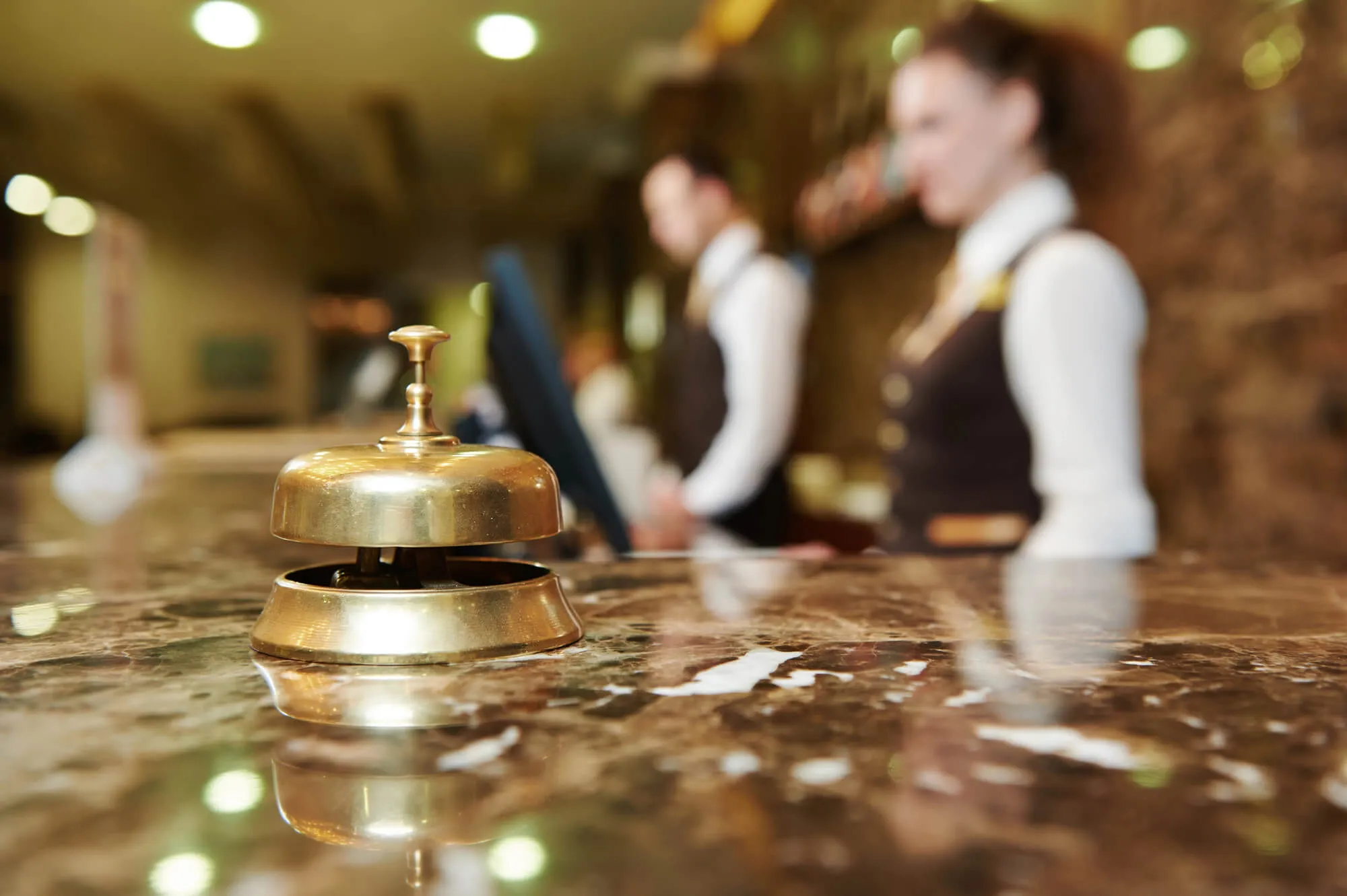 Brass service bell on hotel reception desk with staff in background